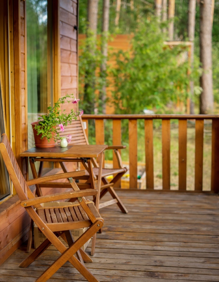 Terrasse en bois avec table pliante, chaises et pot de fleurs devant un chalet